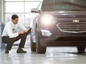 Chevrolet technician kneeling next to a Chevrolet vehicle presumably inspecting the tires.