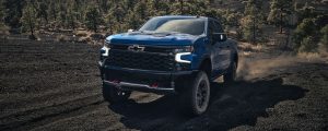 A blue 2022 Chevrolet Silverado 1500 driving towards us on a dirt road.