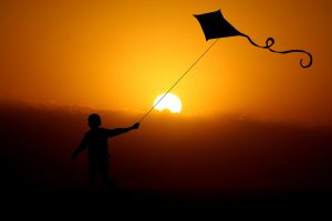 A child flying a kite with the sun setting in the background.