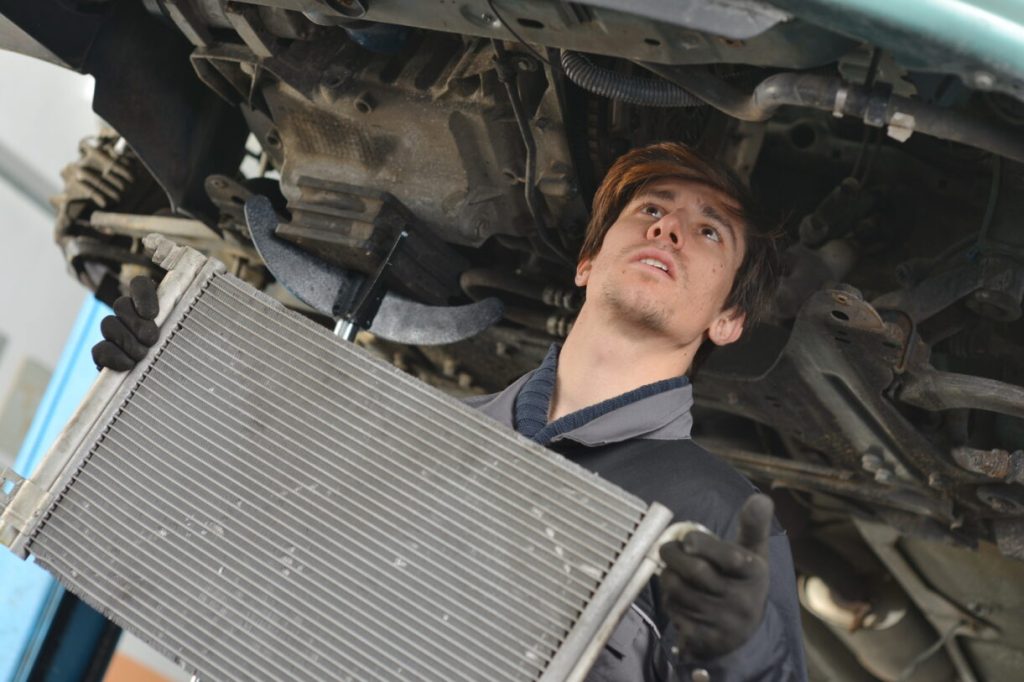 An auto repair technician installing a vehicle radiator.