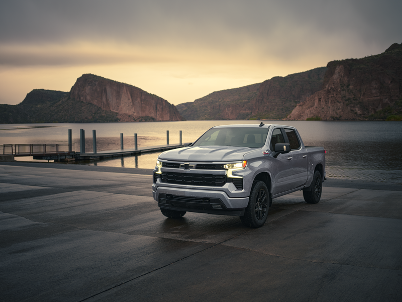A Chevrolet Silverado 1500 parked by a scenic lake at sunset, with mountains in the background.