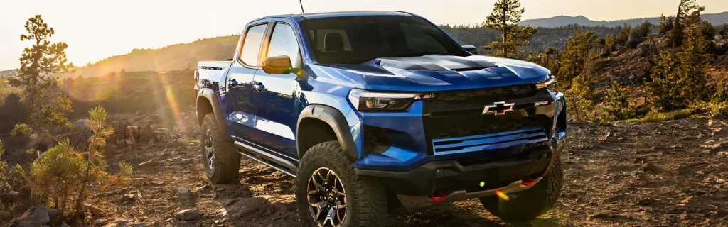 Blue Chevrolet Colorado ZR2 pickup truck tackling rugged mountain terrain at sunset.