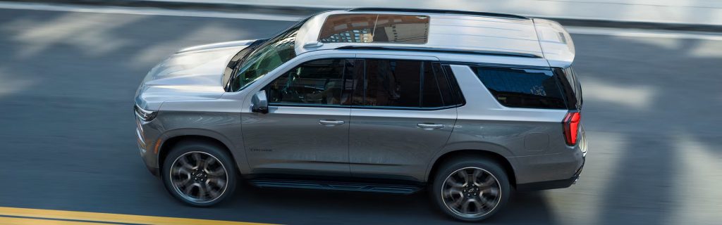 White Chevrolet Tahoe SUV driving on a city road with roof cargo box