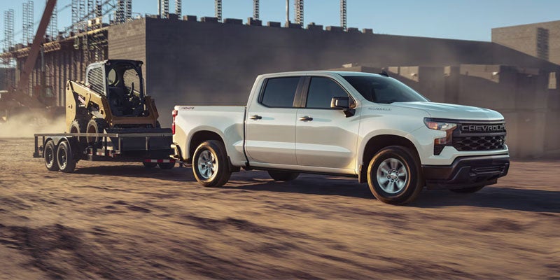 White Chevrolet pickup truck towing construction equipment at a job site
